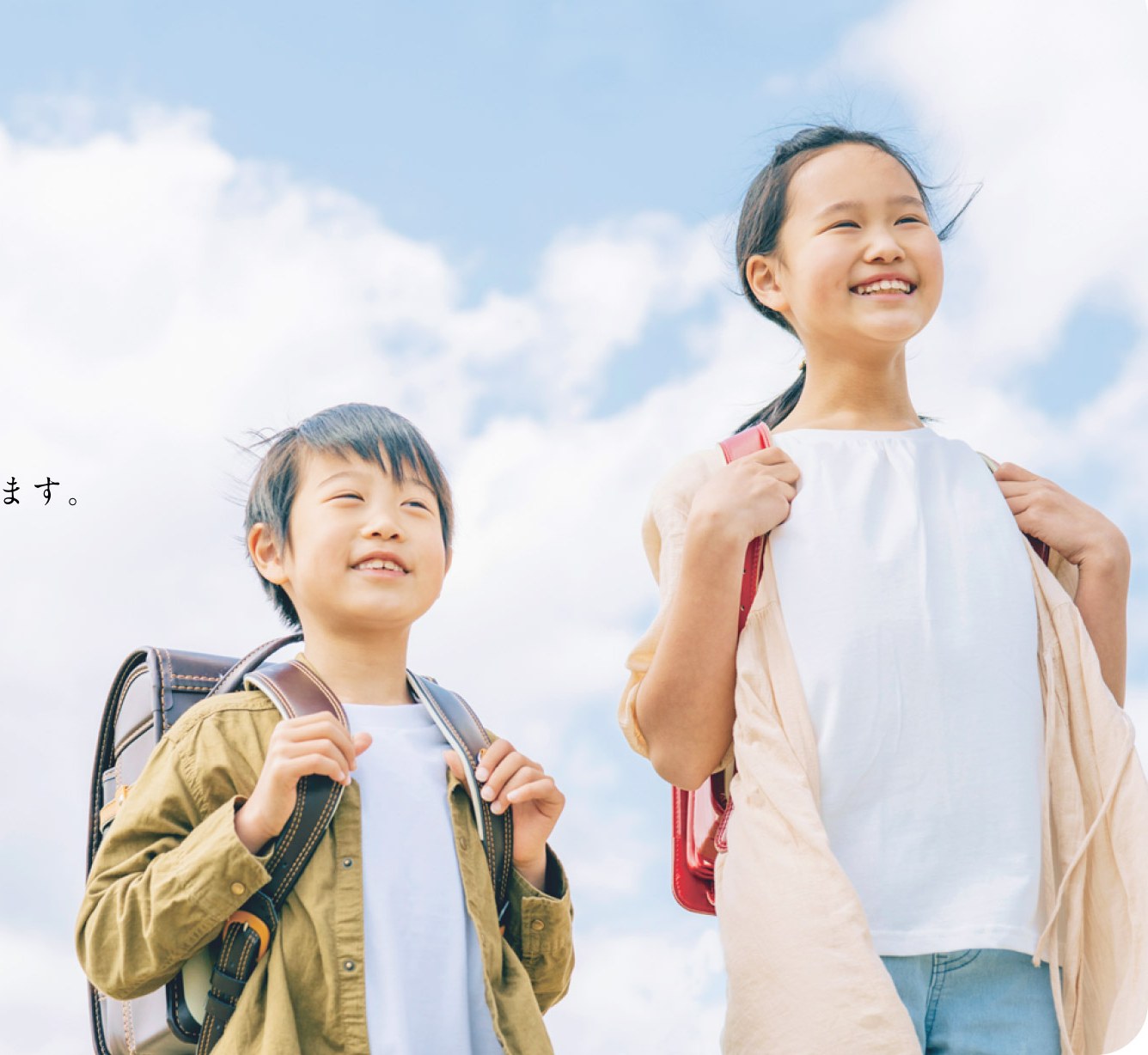 ランドセルを背負い、空の下で笑顔を見せる子どもたち